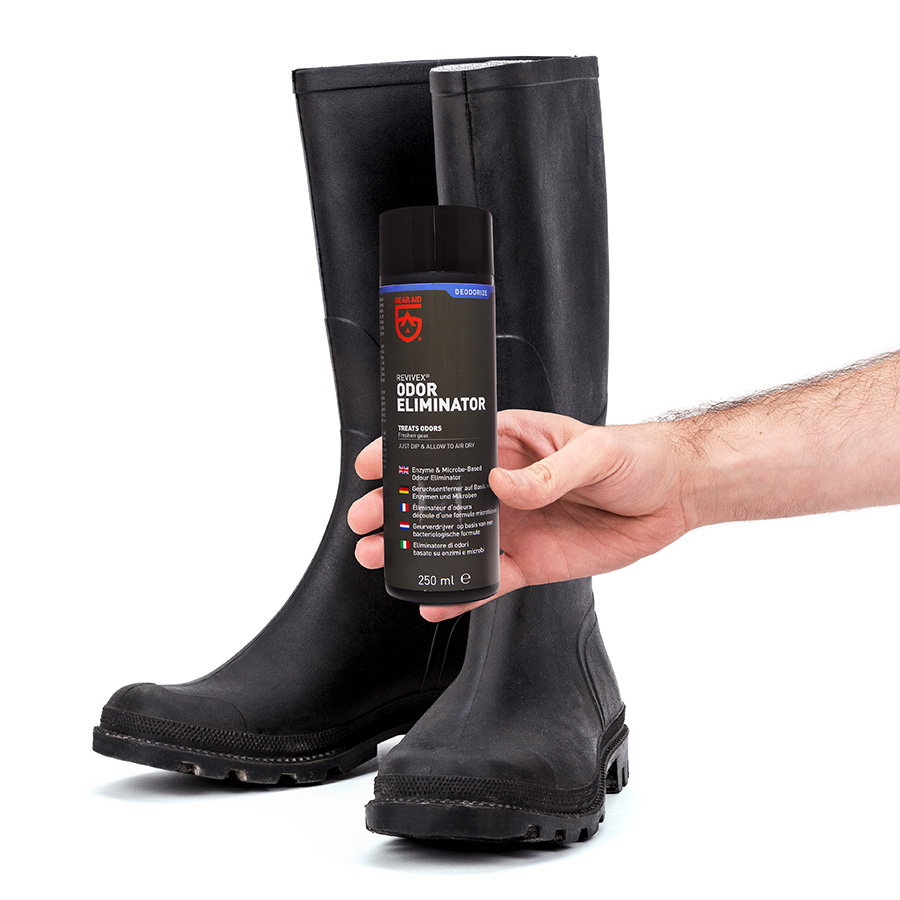 Odor Eliminator mit Stiefel Hand hält Odor Eliminator Flasche vor schwarzen Gummistiefeln