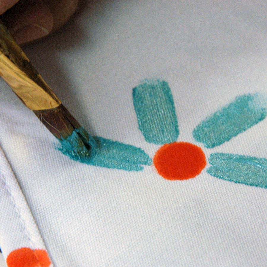 Jacquard Lumiere Metallic and Pearlescent Paint 236 ml Brush painting a flower with turquoise petals and an orange centre on white fabric
