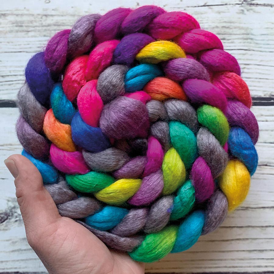 Jacquard Acid Dye Textilfarbe für Wolle und Seide Hand hält aufgerollten Kammzug in Regenbogenfarben